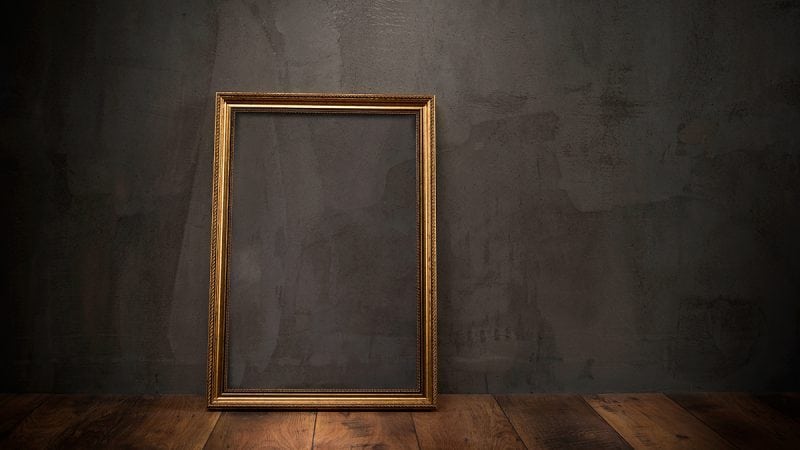 Empty gold frame leaning against a dark wall