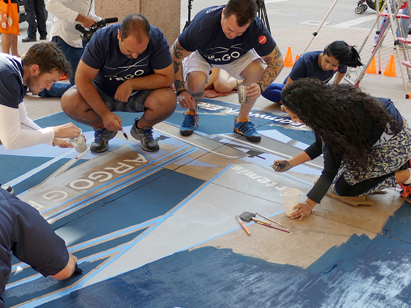 Argo employees working together to paint an intricate design on a sidewalk