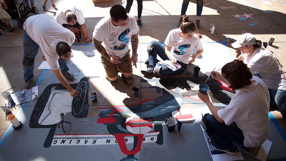 People painting race car with sidewalk chalk during San Antonio's Chalk It Up