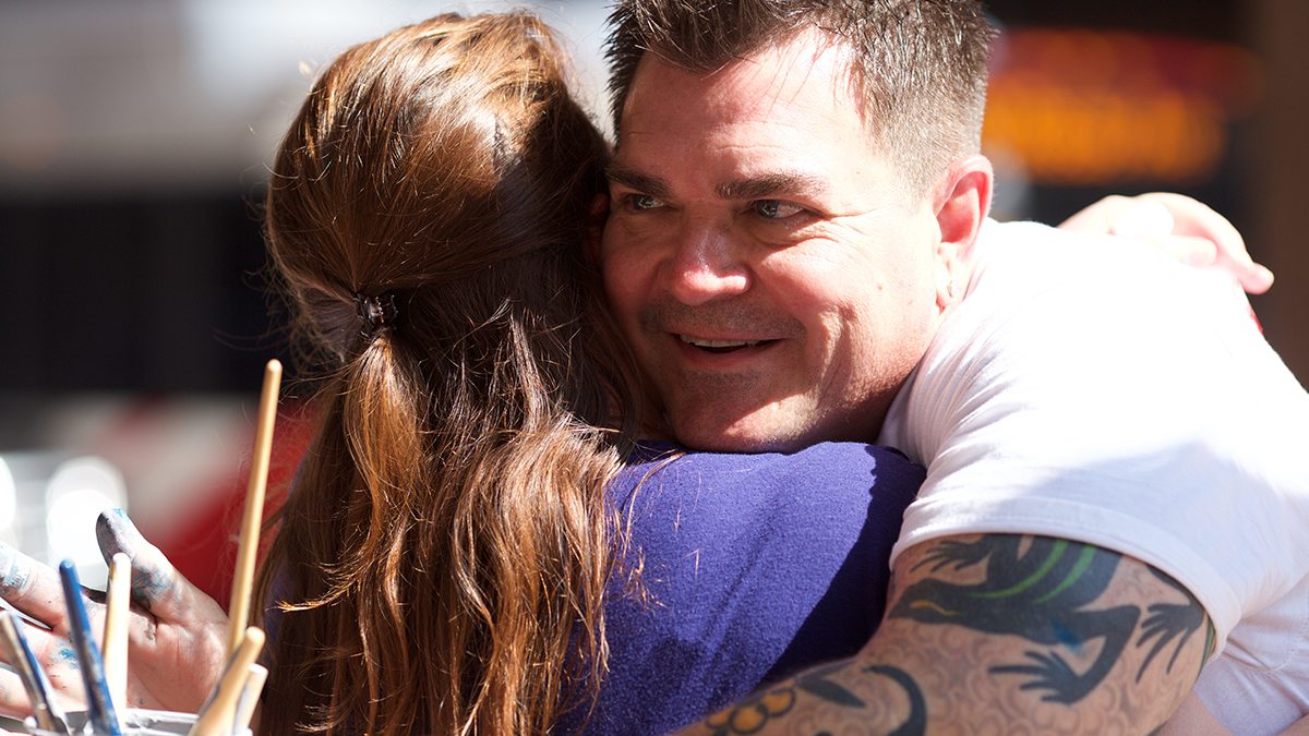 Man with tattooed arms hugging a young woman at San Antonio's Chalk It Up