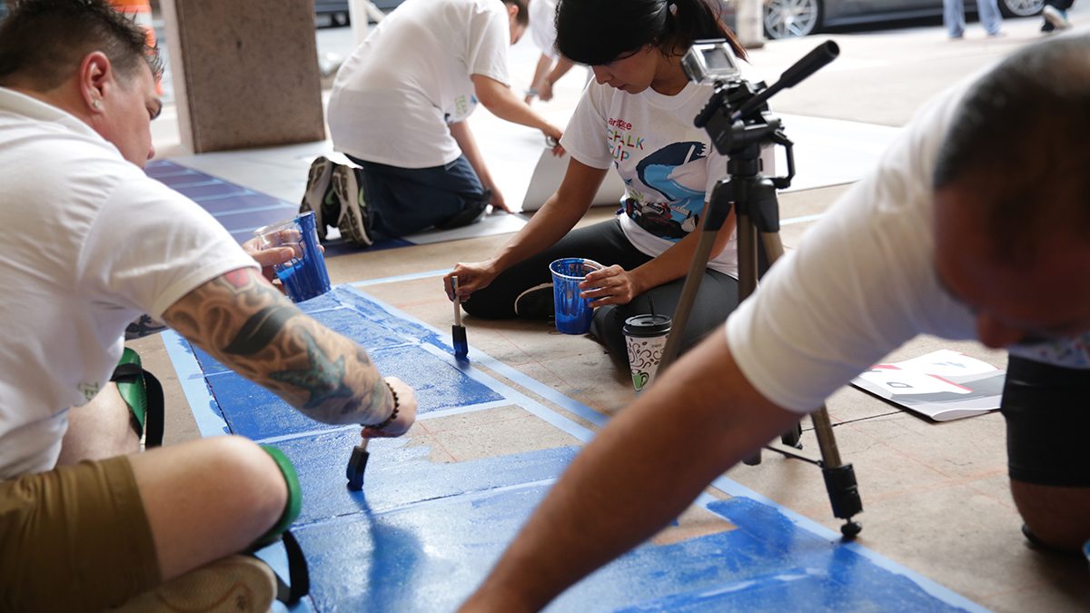 Individuals filling in blue paint during San Antonio's Chalk It Up event