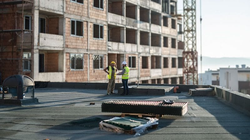 Two men in hard hats standing on the roof of a building under construction.
