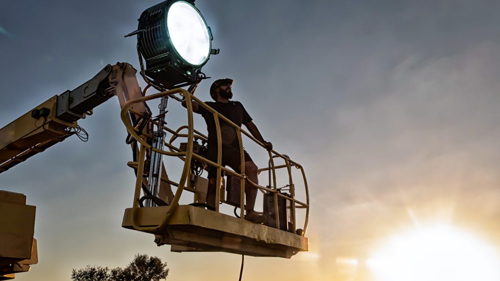Man standing in a cherrypicker operating a large spotlight