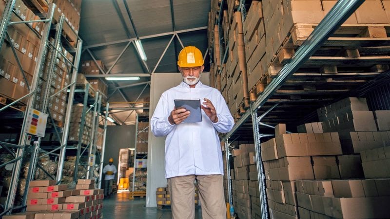 Warehouse employee using mobile device while standing next to a row of boxes
