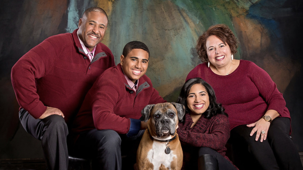 Family in maroon sweaters posing with their dog in a portrait studio