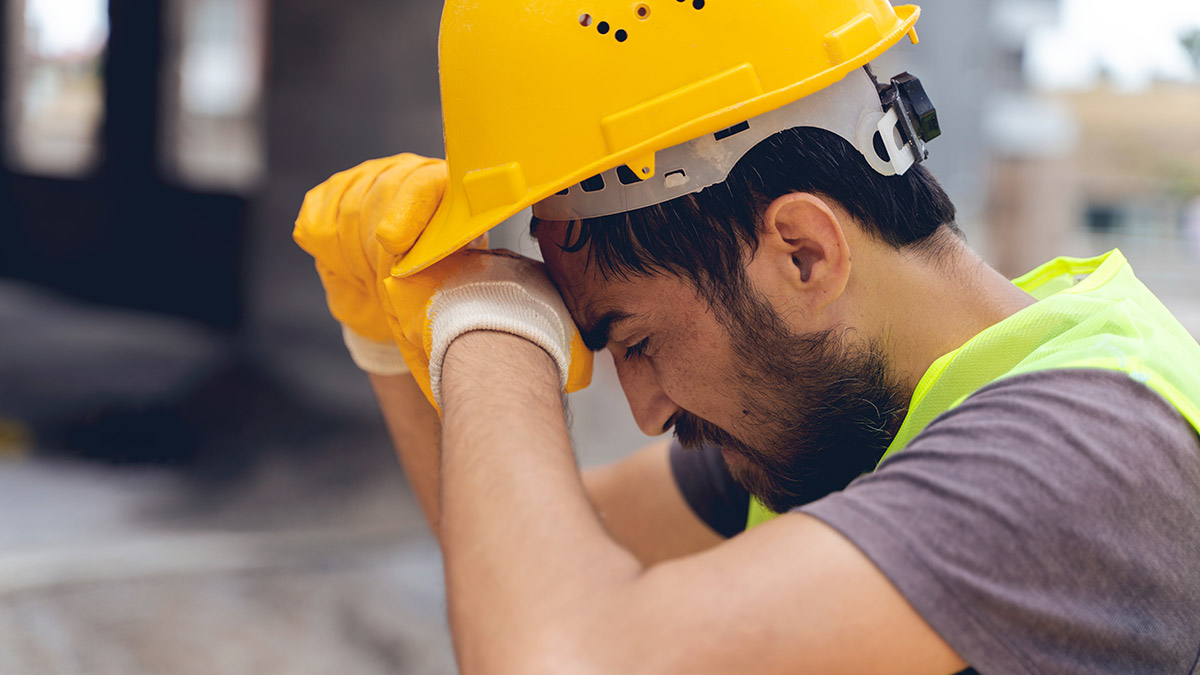 Young construction worker tipping back his hard hat and wiping sweat from his brow.
