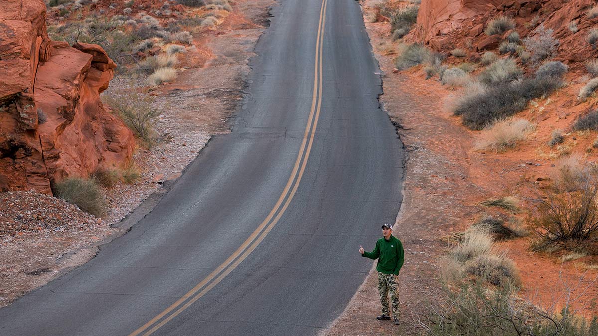 Neal Lee standing along a deserted road with his thumb out as if hitchhiking.