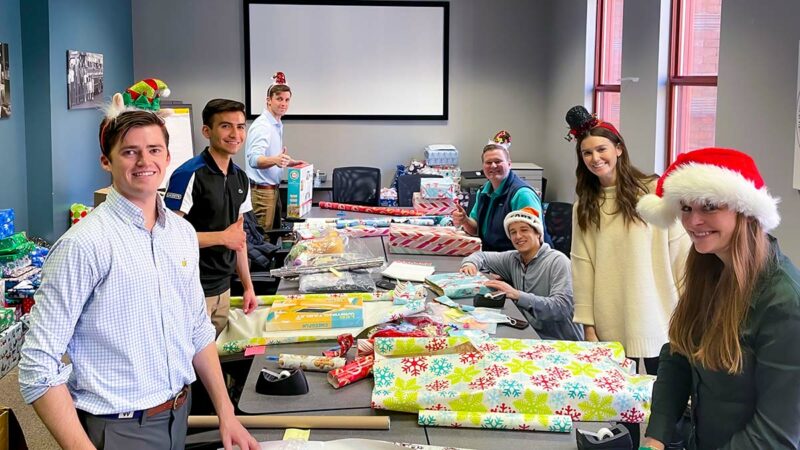 Argo Surety team members stand around a table, smiling, wrapping gifts